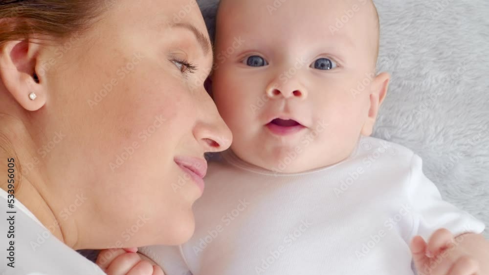 Happy newborn baby with his mother. Healthy newborn baby in a white t-shirt with mom. Closeup Faces of the mother and infant baby. Cute Infant boy and parent, top view. Slow motion. Happy family Happy newborn baby with his mother. Healthy newborn baby in a white t-shirt with mom. Closeup Faces of the mother and infant baby. Cute Infant boy and parent, top view. Slow motion. Happy family