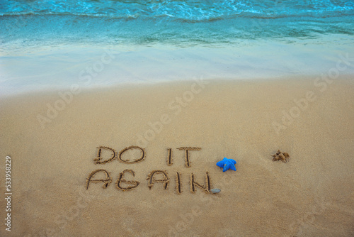 Do it again  written in the sand on the beach with the sea washing up the shore