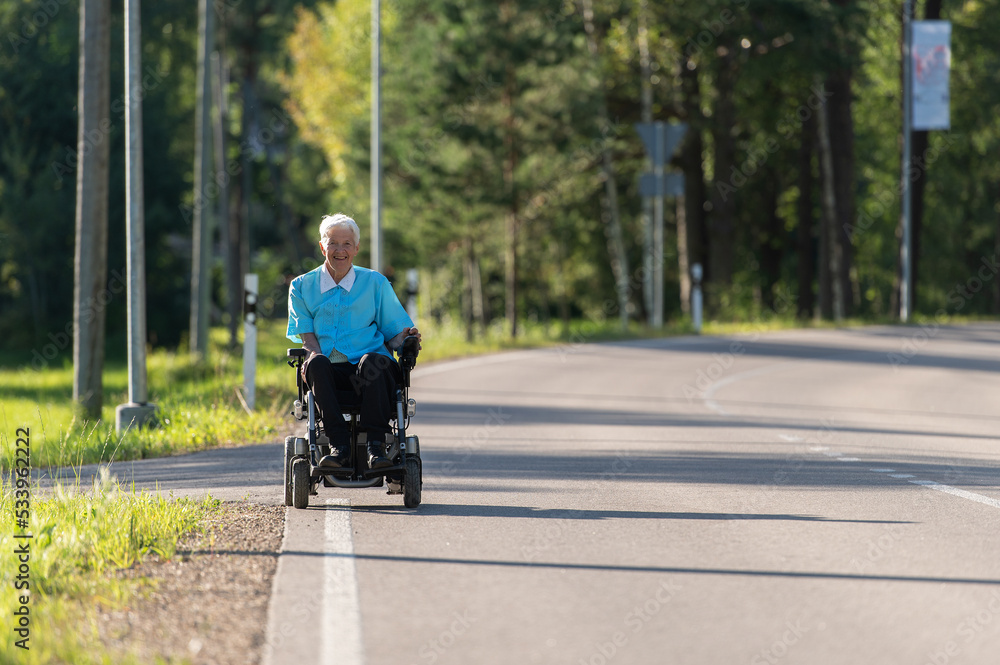 Fototapeta premium Smiling disabled old woman in a wheelchair on the highway