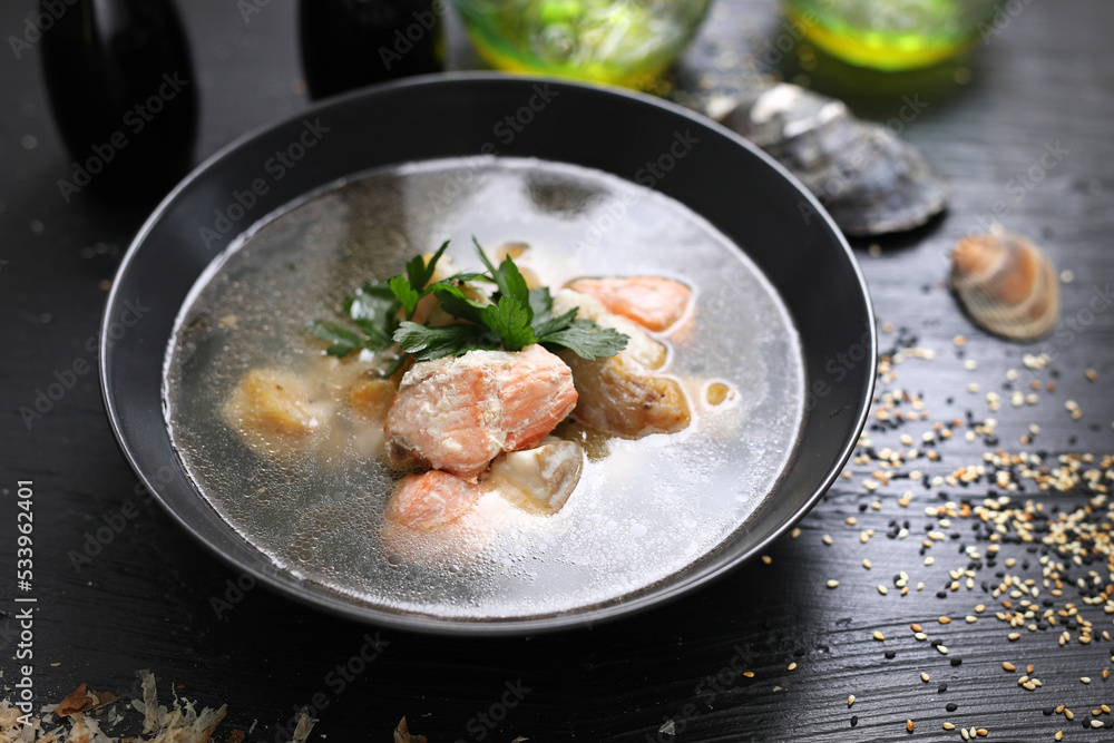 Fish soup with salmon. Black bowl with fish broth soup, on a black table, top view.