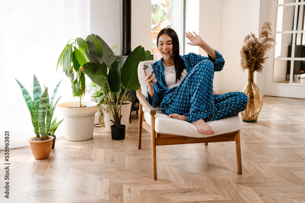 Young asian girl using mobile phone while sitting in chair at home Young asian girl using mobile phone while sitting in chair at home