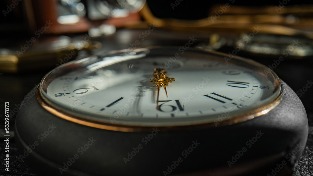 Silver antique pocket watch with a white dial, golden hands and shiny reflective glass with shadow. Macro shot of old gray round pocket watch and vintage camera on a blurred dark background.