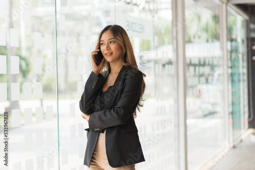 Using mobile, cheerful young asian business woman working at working place.