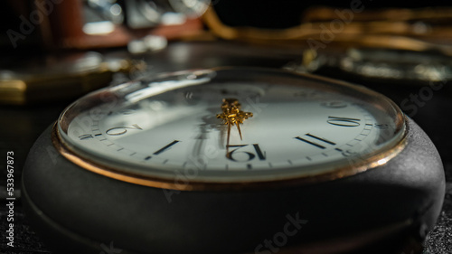 Silver antique pocket watch with a white dial, golden hands and shiny reflective glass with shadow. Macro shot of old gray round pocket watch and vintage camera on a blurred dark background.