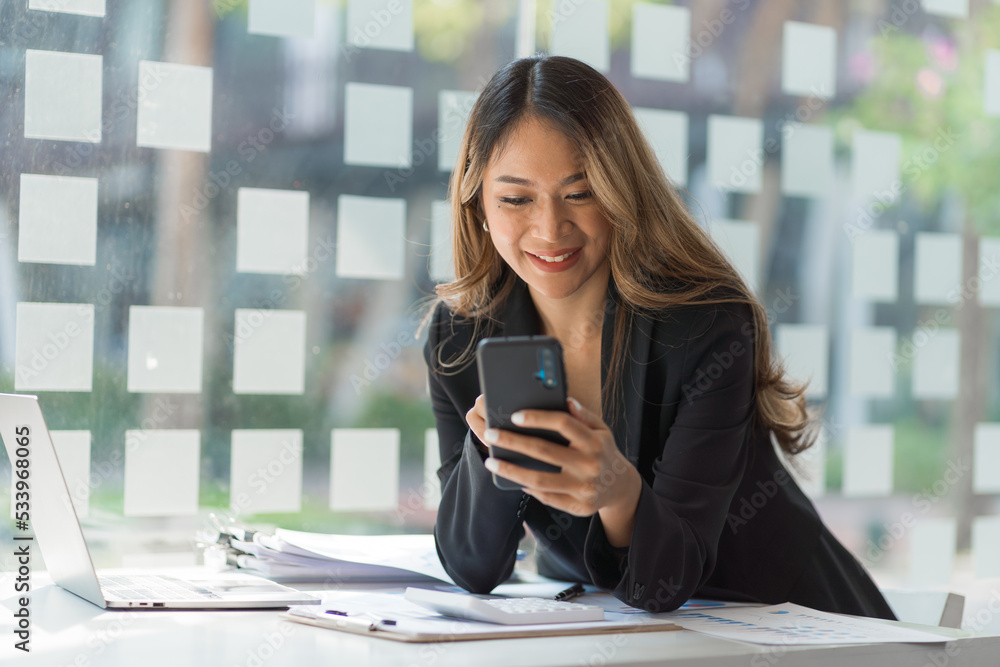 Obraz premium Using mobile, cheerful young asian business woman working at working place.