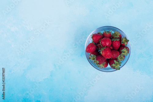 Red strawberries in a glass cup on blue background on the right