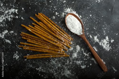 Uncooked spaghetties with flour in a wooden spoon