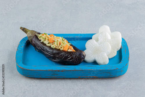 Rice in eggplant next to cross shaped radish on the board , on the marble background photo