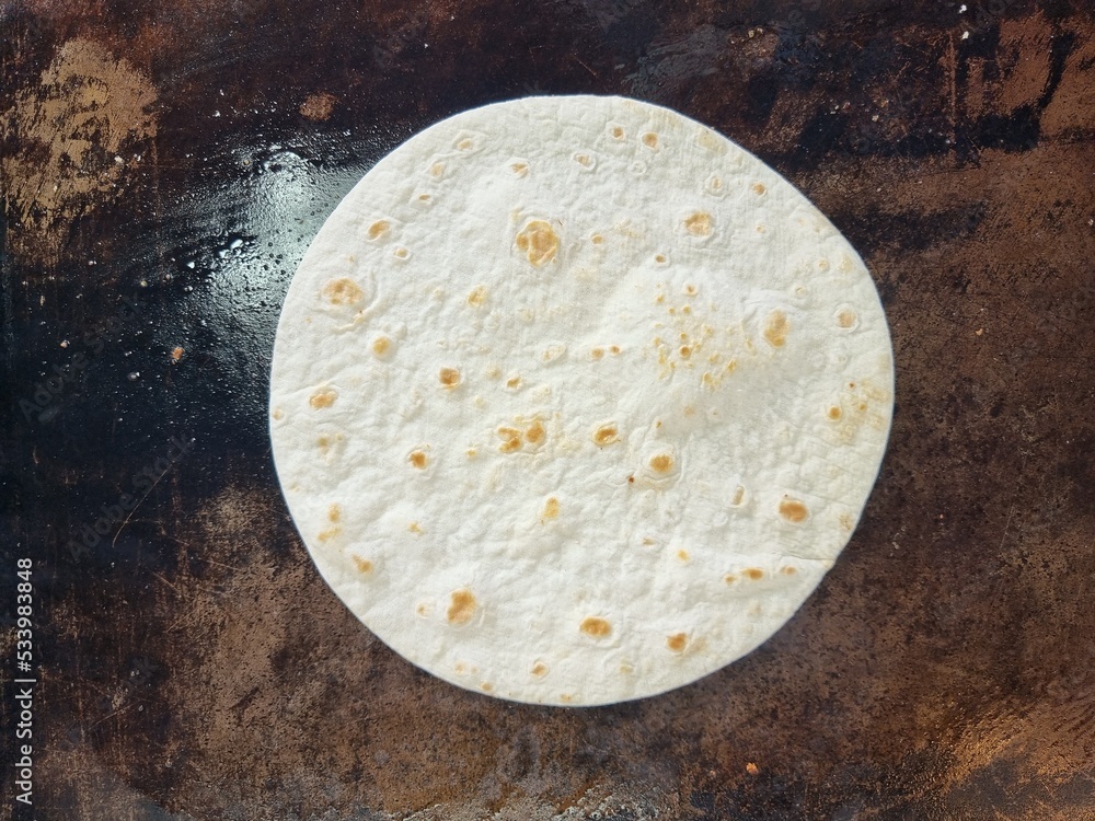 Plain tortilla wrap (Roti) on the iron flat pan. Plain tortilla wrap (Roti) on the iron flat pan.