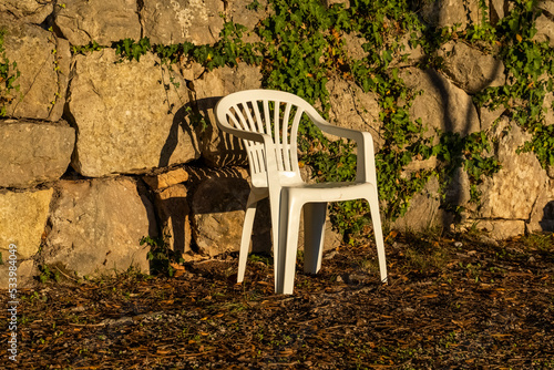 a white plastic chair thrown out by people on the street near the forest. Pollution of the environment by plastic, A summer plastic chair stands in nature.