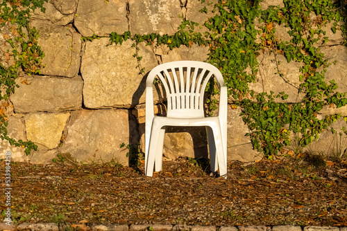 a white plastic chair thrown out by people on the street near the forest. Pollution of the environment by plastic, A summer plastic chair stands in nature.