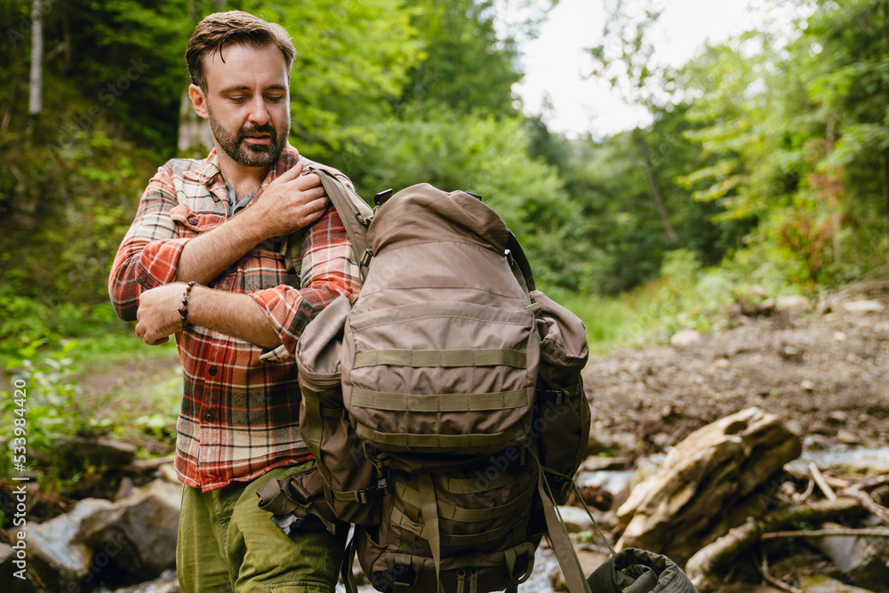 Young white man holding backpack while hiking in forest