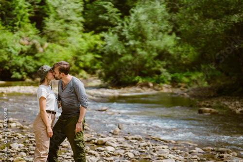 White young couple kissing each other while hiking by river in nature