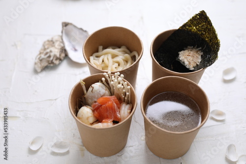Seafood ramen soup ingredients in take-away boxes. Fish ramen components in carton containers on a white background.