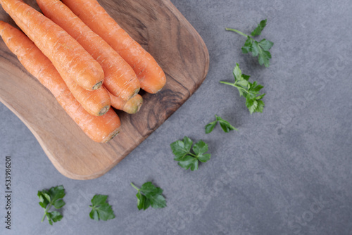 Raw carrots with greens on the cutting board , on the marble background photo