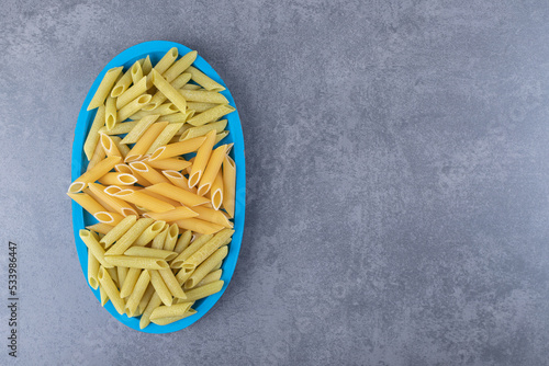 Raw green and yellow penne pasta on blue plate