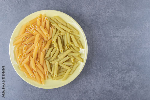 Raw green and yellow penne pasta on yellow plate