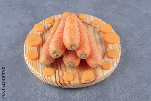 Whole and sliced carrots in the wooden plate , on the marble background photo