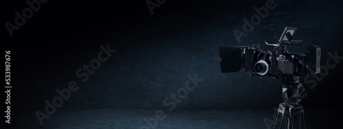 Digital movie camera in dark concrete room with light. Tv documentary or movie production banner background