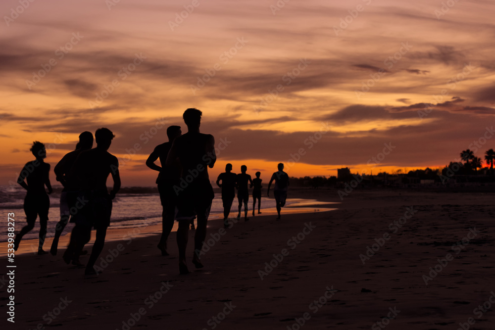 Silhouette of young fitness boys model of a soccer beach team jogging, running at sunrise sea in Rome Italy in a romantic sunset Silhouette of young fitness boys model of a soccer beach team jogging, running at sunrise sea in Rome Italy in a romantic sunset