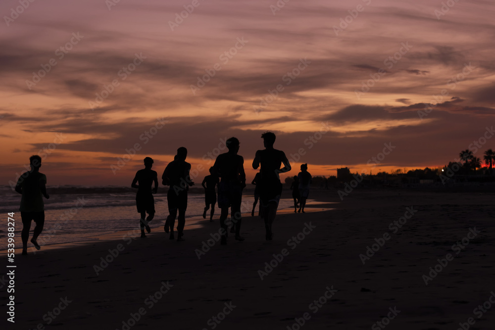 Silhouette of young fitness boys model of a soccer beach team jogging, running at sunrise sea in Rome Italy in a romantic sunset