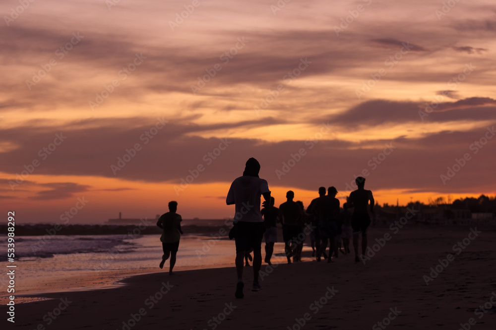 Silhouette of young fitness boys model of a soccer beach team jogging, running at sunrise sea in Rome Italy in a romantic sunset Silhouette of young fitness boys model of a soccer beach team jogging, running at sunrise sea in Rome Italy in a romantic sunset