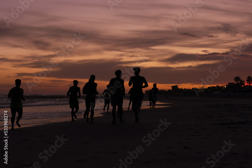 Silhouette of young fitness boys model of a soccer beach team jogging, running at sunrise sea in Rome Italy in a romantic sunset © fabrizio