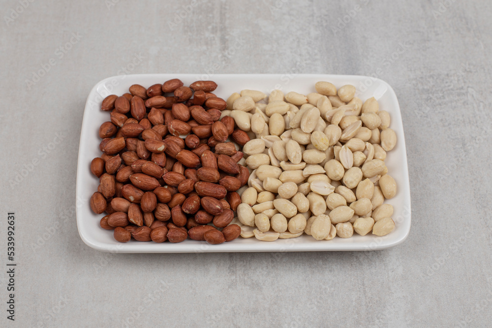 Pile of peeled and unpeeled peanuts on white plate Pile of peeled and unpeeled peanuts on white plate
