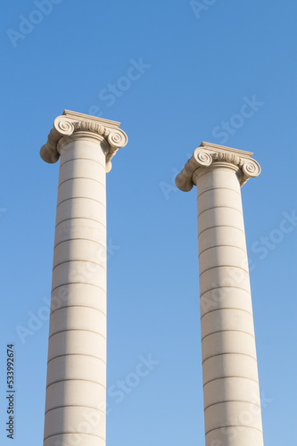 Two columns of the famous "Cuatro Columnas" or "Quatre columnes" of Barcelona (Catalonia, Spain). Two white columns or pillars with the blue sky in the background.