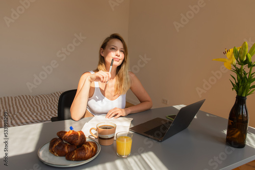 Pensive freelancer holding pen near breakfast and gadgets at home.