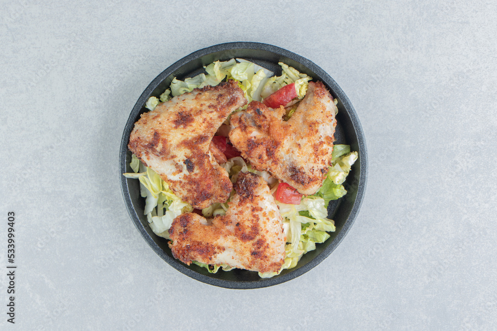 A black bowl with fried chicken legs and vegetable salad A black bowl with fried chicken legs and vegetable salad