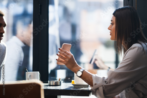 Friends in a restaurant talking smiling and showing pictures on a phone. Business colleagues having a meeting after work at a cafe bar.