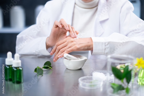 A Female scientists is testing and sampling results of eco skin care, organic lotion and natural cosmetics on hand skin in laboratory for essential, research, and treatment. Concept of beauty product.