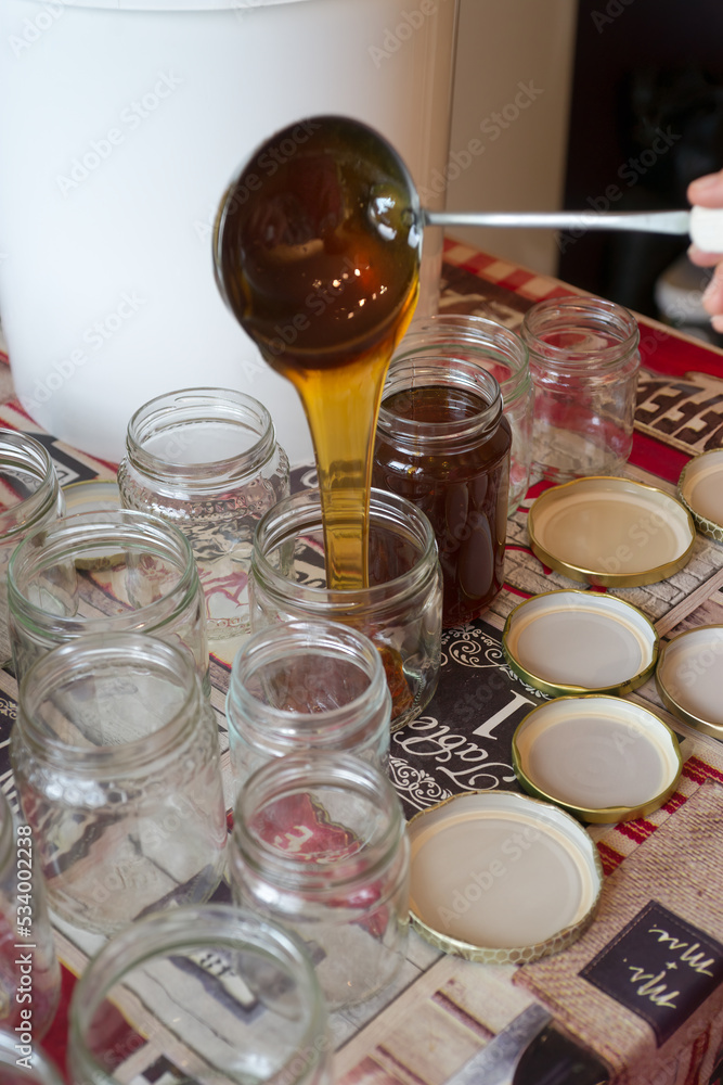 Filling of glass jars of honey on a table Filling of glass jars of honey on a table