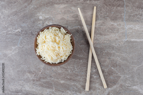 A small bowl of shredded pasta next to the chopstick , on the marble background