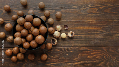 Macadamia nuts in bowl and on wooden table. Whole and open nuts, shell fragments on a brown background