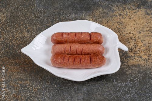 Roasted tasty sausages on leaf shaped plate photo