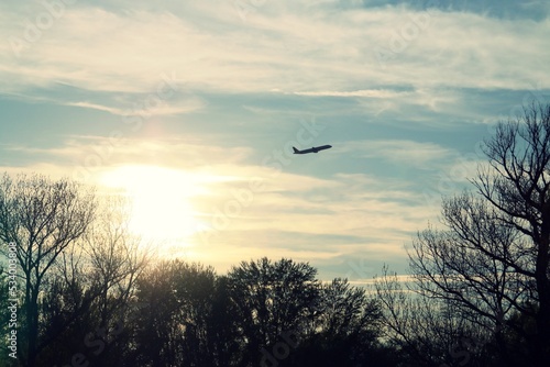 Silueta de un avión sobre la silueta de los árboles al atardecer. Silueta de un avión de pasajeros que despegó del aeropuerto Adolfo Suarez Madrid Barajas en España con los últimos rayos del sol. photo