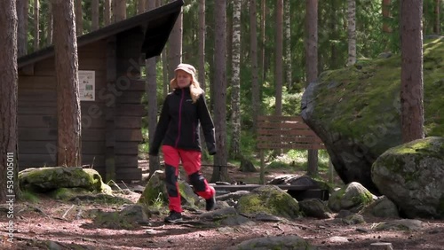 Woman walking towards the camera in front of campfire site and lean-to shelter of Sorsakolu in Evo Hiking Area, Hämeenlinna, Finland. photo