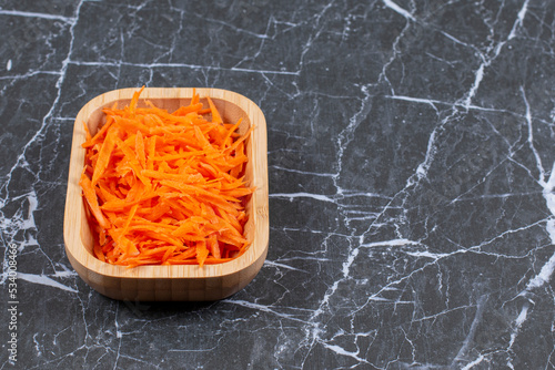 Close up photo of Grated fresh carrot in a brown wooden bowl