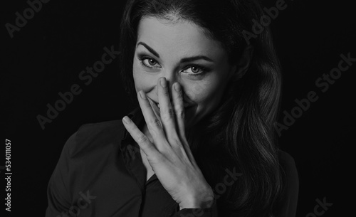 Fotografi Happy chuckling fun business beautiful woman covering the mouth and closed nose the hand on shirt on black background with empty copy space
