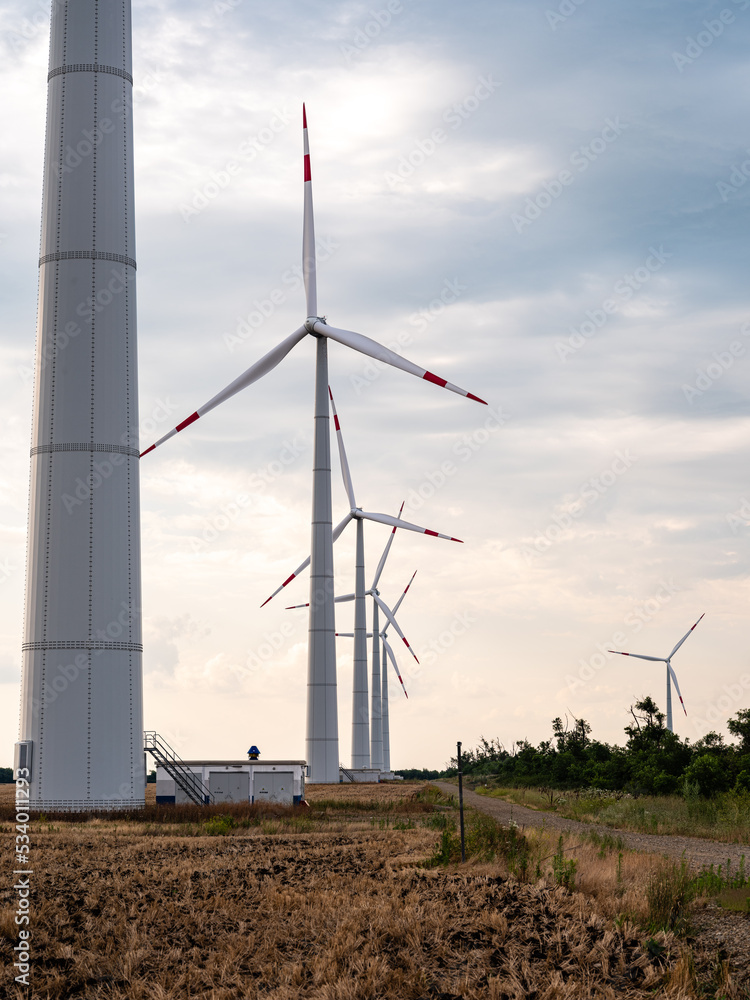 Towers of wind turbines with rotating blades at sunset against cloudy sky. Close-up. Adyghe wind farm from many towers of wind turbines in field. Wind power complex of Rosatom. Towers of wind turbines with rotating blades at sunset against cloudy sky. Close-up. Adyghe wind farm from many towers of wind turbines in field. Wind power complex of Rosatom.