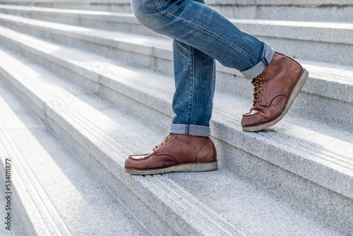 Close up a Young fashion man's legs in blue jeans and brown boots on the walk down the concrete stairs, lifestyle men's fashion