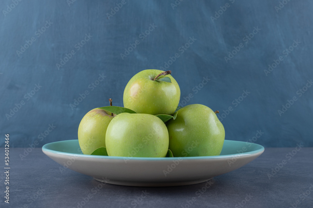 Close up photo of green apple on plate over grey background Close up photo of green apple on plate over grey background