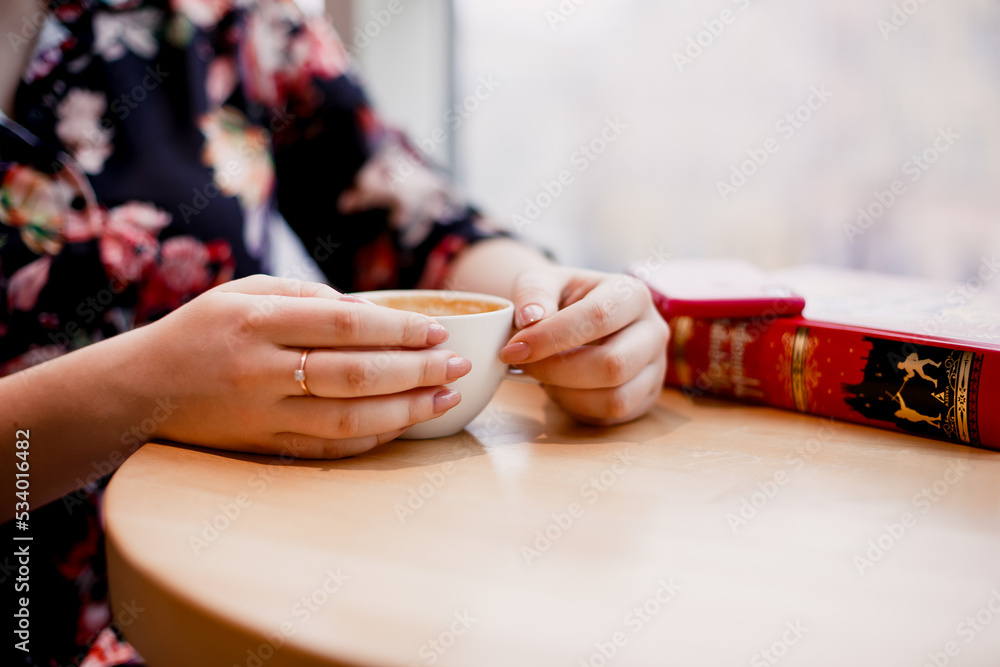 Naklejka premium Kyiv, Ukraine. August 5, 2022. A girl in a cafe holds a cup of coffee and reads the book 