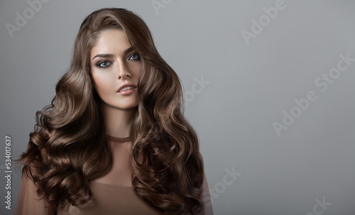 Portrait of a beautiful girl with luxurious curly long hair. Gray background.
