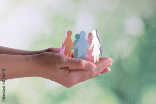Woman holding paper human figures on blurred background, closeup. Diversity and Inclusion concept photo