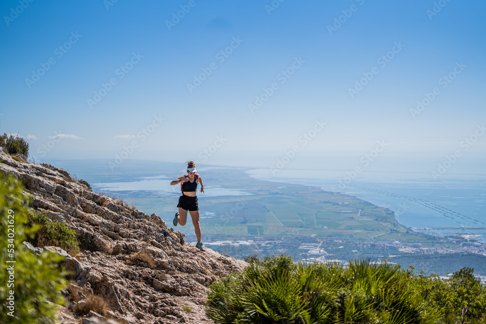 Blonde caucasian woman with a visor running on top of a mountain with a view