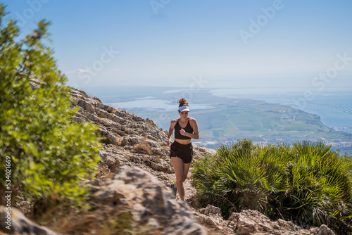 Blonde caucasian woman with a visor running on top of a mountain with a view