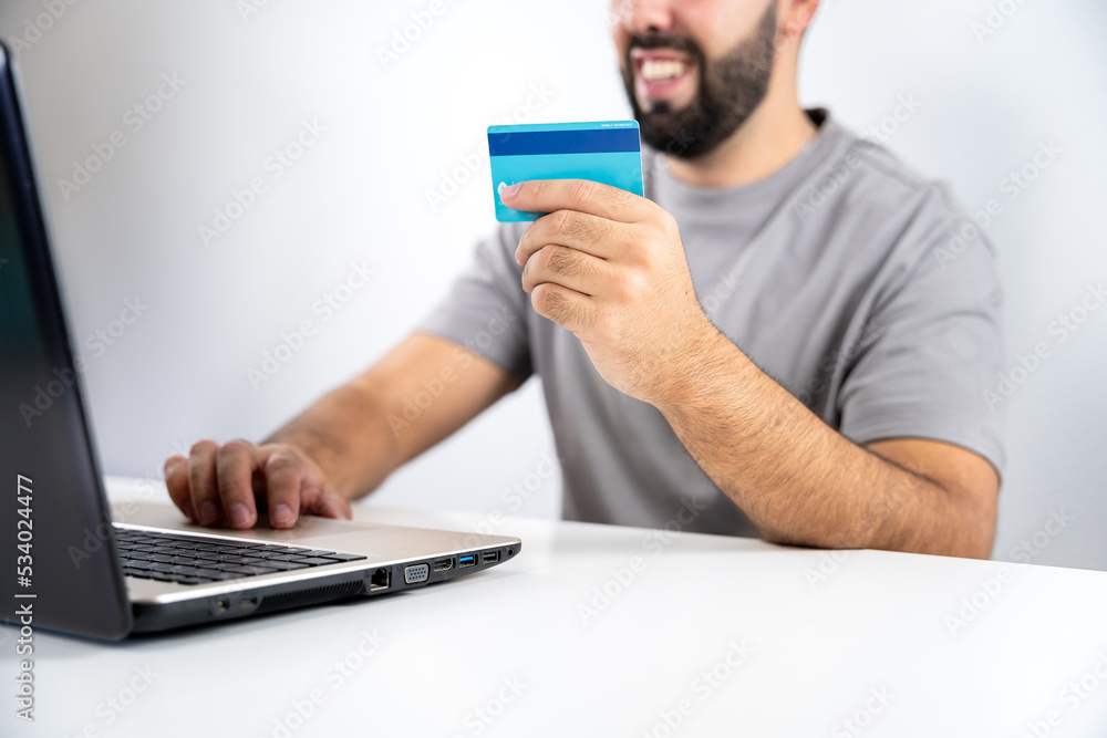 Unrecognizable young man with computer and holding card to shop online from home - concept shopping, black friday, cyber monday, sales, christmas